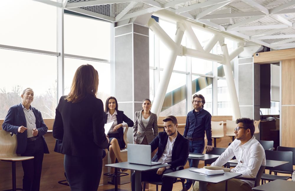 Various businessmen listen to female business leader during corporate meeting or training lecture.